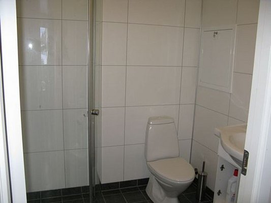 Helles Badezimmer in Nord-Norwegen mit Dusche, WC und Waschbecken. Moderne, schlichte Fliesen in Weiß gestalten eine funktionale Atmosphäre. Ideal für einen komfortablen Aufenthalt während eines Angelurlaubs.