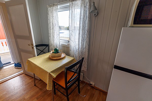 Gemütliche Küche in norwegischem Ferienhaus auf Hitra. Holzvertäfelung, Fenster mit Aussicht, gelb karierter Tisch. Ideal für entspannte Angelurlaube, umgeben von unberührter Natur und herrlichen Angelmöglichkeiten in Norwegen. Perfekt für Abenteuerlustige und Erholungssuchende.