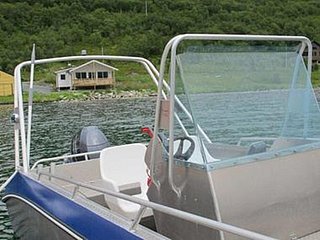 Modernes Angelboot im klaren Wasser eines norwegischen Fjords, umgeben von grünen Hügeln und einer gemütlichen Hütte – ideal für Angelreisen und Abenteuer in Südwest-Norwegen.