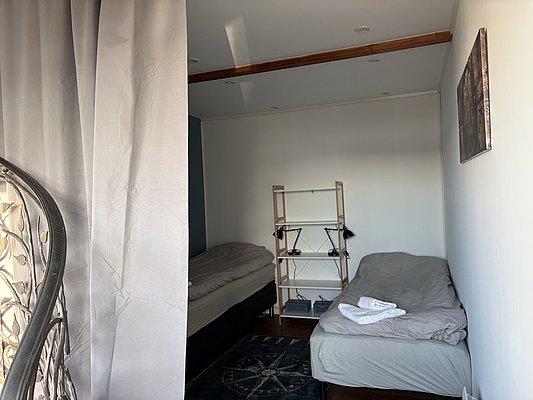 Gemütliches Zimmer in Nord-Norwegen mit zwei Einzelbetten, Regal und Teppich. Ideal für Angelurlauber, die Erholung in der Nähe von reichhaltigen Fischgründen suchen. Perfekt für Abenteuer und Entspannung in skandinavischem Ambiente.