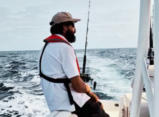 Ein Angler sitzt entspannt auf einem Boot vor São Vicente, Kapverden, bereit zum Meeresangeln. Die weite Meereslandschaft und der blaue Himmel versprechen ein spannendes Angelabenteuer.