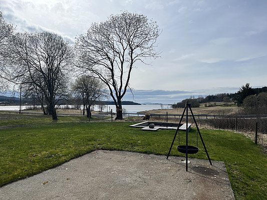 Grüne Wiesen und karge Bäume vor norwegischer Küstenlandschaft auf Hitra. Der Ausblick lädt zum Angelurlaub ein; klare Luft und weite Horizonte bieten Entspannung und Abenteuerlust in der Natur. Ideal für Angler und Naturfreunde.