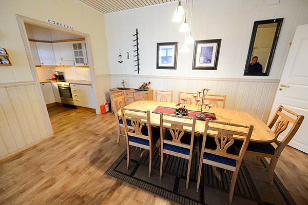 Gemütliches Esszimmer in Nord-Norwegen: Holztisch mit acht Stühlen, skandinavisches Design, angrenzende helle Küche. Perfekte Unterkunft für Angelreisende, die Komfort und Funktionalität suchen.