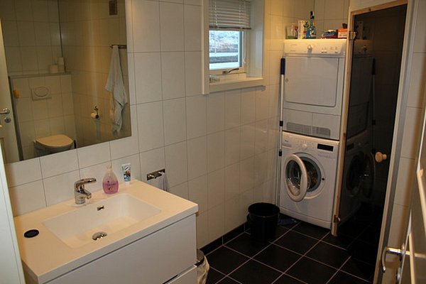 Modernes Badezimmer in Nord-Norwegen mit Waschbecken, Spiegel und Waschmaschine. Helle Fliesenwände und dunkler Fliesenboden bieten eleganten Kontrast. Praktische Ausstattung für Komfort nach einem erfolgreichen Angeltag.