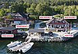 Luftaufnahme einer idyllischen Küstenunterkunft in Südwest-Norwegen mit traditionellen roten Holzhäusern, eigenem Bootssteg und Hot Tub. Perfekt für Angelurlauber, die Erholung und Abenteuer inmitten beeindruckender Natur suchen. Keywords: Südwest-Norwegen, Angelreise, Küstenunterkunft.