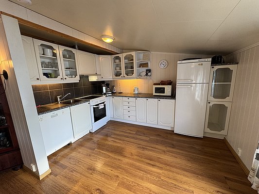 Gemütliche, voll ausgestattete Küche in Unterkunft bei Hitra, Norwegen. Helle Einbauschränke, moderner Ofen, Mikrowelle und Kühlschrank auf Holzfußboden. Ideal für Angler auf Angelurlaub mit Fokus auf Komfort und Selbstversorgung.