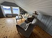 Gemütlicher Wohnbereich mit grauem Sofa, Holzfußboden und großen Fenstern mit Meerblick in Hitra, Norwegen. Ideal für entspannenden Angelurlaub. Heizung und Ventilator sorgen für Komfort bei jedem Wetter.