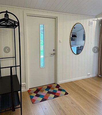 Gemütliches Ferienhaus in Hitra, Norwegen: Helle, freundliche Inneneinrichtung mit Holzfußboden, bunter Teppich, stilvolle Garderobe und ovaler Spiegel. Ideal für entspannende Angelurlaube in atemberaubender Naturkulisse.