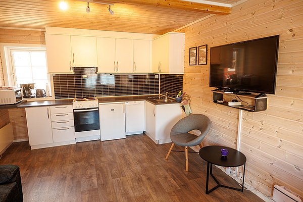 Gemütliche, moderne Küche in Norwegens Nordland mit Holzverkleidung, Küchenzeile, TV und Sitzbereich. Ideal für Angelurlauber, die Komfort nach spannenden Angelausflügen suchen. Perfekte Kombination aus Tradition und Moderne.