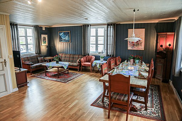 Gemütliches Wohnzimmer in Nord-Norwegen: rustikale Einrichtung, Holzmöbel, großer Esstisch, bequeme Sofas, helle Fenster. Perfekt für entspannte Abende nach einem erfolgreichen Angeltag. Ideal für Angelurlaub und Naturerlebnisse in malerischer Umgebung.