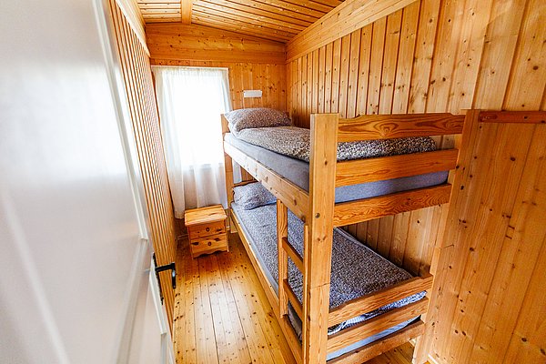Gemütliches Holzschlafzimmer mit Etagenbett in einer Hütte in Hitra, Norwegen. Ideal für Angelurlaub. Helle Einrichtung, Fenster mit Vorhang, kleiner Holztisch. Perfekt für naturverbundene Erholung.