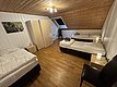 Gemütliches Schlafzimmer in Hitra, Norwegen mit Holzdielen, drei Betten, Dachschräge und sanfter Beleuchtung. Ideal für erholsame Angelurlaube mit Freunden. Entspannte Unterkunft nach erfolgreichen Tagen beim Meeresangeln.