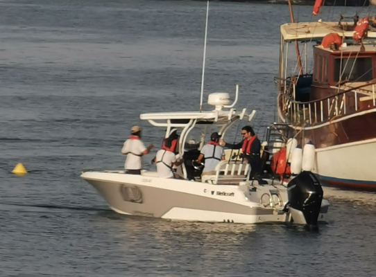 Motorboot mit mehreren Personen im Hafen von Sao Vicente, Kapverden. Blaues Meer, angrenzendes größeres Boot. Maritime Szene ideal für Angelreisen und Erkundungstouren. Authentisches Küstenerlebnis auf Kap Verden.