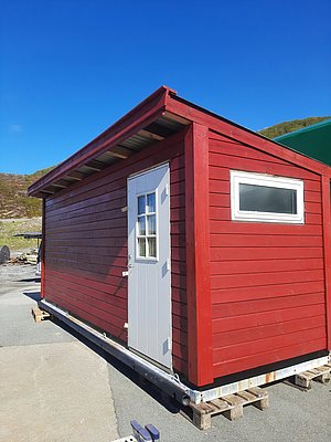 Rotes Holzhaus in Hitra, Norwegen, unter klarem blauem Himmel. Traditionelle skandinavische Architektur, idealer Ausgangspunkt für Angelurlaube. Erleben Sie nachhaltigen Tourismus in natürlicher Schönheit. Perfekt für Naturliebhaber und Abenteuerlustige.