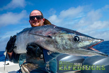 Ein begeisterter Angler hält stolz einen großen Wahoo-Fisch auf einem Boot vor der Küste Tansanias. Der klare Himmel und das tiefblaue Meer bieten eine atemberaubende Kulisse für diesen erfolgreichen Angeltrip.