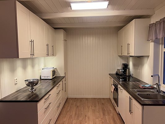 Einladende Küche in Nord-Norwegen: Moderne Einrichtung mit weißem Holzdekor, dunklen Arbeitsflächen und gut ausgestatteten Geräten. Perfekt für gemütliche Kochabende nach ereignisreichen Angelabenteuern. Ideal für Angelreisende, die Komfort und Funktionalität schätzen.