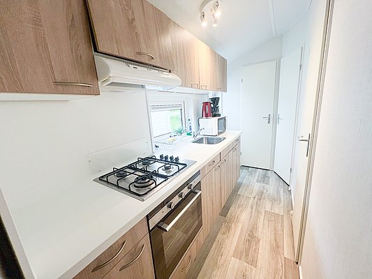 Kompakte moderne Küche in Nord-Norwegen mit Holzschränken, Gasherd, Backofen und weißer Arbeitsfläche. Perfekt ausgestattet für Angler auf Reisen, die in gemütlicher Umgebung kochen möchten. Ideal für Angelurlaub und Komfort.