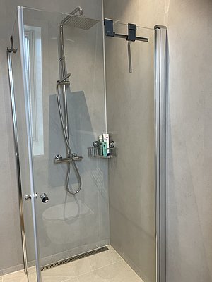 Moderne, helle Duschkabine mit Glaswänden und Regendusche in Hitra, Norwegen. Ideal für Angelurlauber, die nach einem erfolgreichen Tag am Meer entspannen möchten. Stilvolle Ausstattung sorgt für Komfort. Perfekt für Angelreisen zur Erholung.