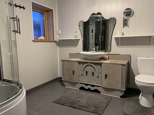 Helles, gemütliches Badezimmer in Nord-Norwegen mit stilvollem Waschtisch, modernen Armaturen und großem Spiegel. Entspanntes Ambiente für Angelurlauber, ideal nach abenteuerlichen Tagen in der nordischen Natur.