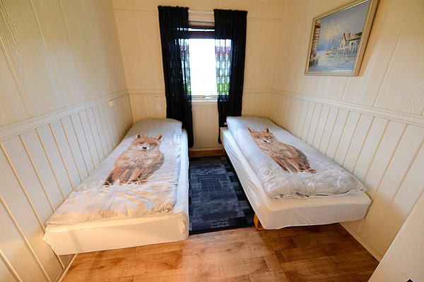 Gemütliches Schlafzimmer in Nord-Norwegen mit zwei Einzelbetten, Fuchs-Bettwäsche, Holzvertäfelung, hellem Holzfußboden und maritimer Wandkunst. Perfekte Unterkunft für Angelreisende, die Komfort und ein naturnahes Erlebnis suchen.