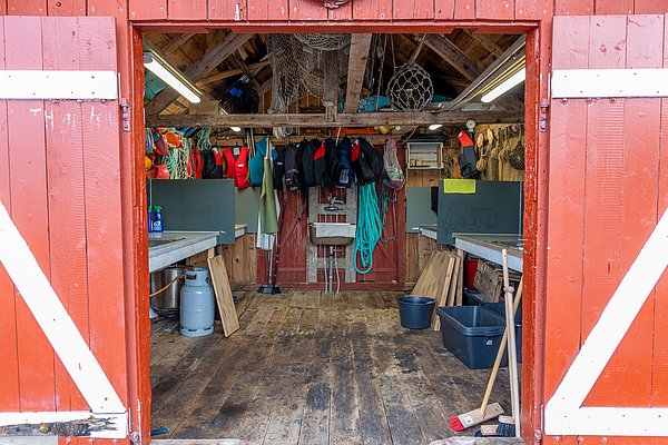 Rotes Holzgebäude in Hitra, Norwegen. Innenansicht zeigt Angelzubehör: Rettungswesten, Netze, bunte Seile. Perfekt für Meeresangeln und Angelurlaub. Ideal für Angler, die Abenteuer und reiche Fangmöglichkeiten suchen. Petri Heil!
