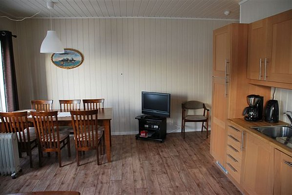 Gemütlicher Wohnbereich in Nordland, Norwegen: Holzküche, Esstisch für sechs Personen, Fernseher. Perfekt für Angelreisen, um nach einem erfolgreichen Tag zu entspannen. Charmante Einrichtung lädt zur Erholung ein.