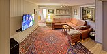 Gemütliches Wohnzimmer in einer Unterkunft in Nordland, Norwegen. Große Ledercouch, persischer Teppich, moderner Flachbildfernseher und dezente Beleuchtung schaffen eine einladende Atmosphäre. Perfekt zum Entspannen nach einem erlebnisreichen Angelurlaubstag.