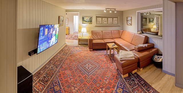 Gemütliches Wohnzimmer in einer Unterkunft in Nordland, Norwegen. Große Ledercouch, persischer Teppich, moderner Flachbildfernseher und dezente Beleuchtung schaffen eine einladende Atmosphäre. Perfekt zum Entspannen nach einem erlebnisreichen Angelurlaubstag.