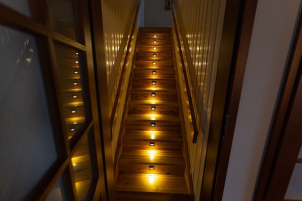Holztreppe in einem norwegischen Haus mit warmen LED-Leuchten entlang der Stufen, die eine gemütliche Atmosphäre schaffen. Ideal für einen Angelurlaub in Nord-Norwegen, kombiniert Komfort und traditionelle Bauweise.