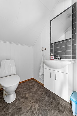 Helles, modernes Badezimmer in Nord-Norwegen mit weißen Wänden, grauen Fliesen, WC und Waschbecken. Perfekt für deinen Angelurlaub – komfortabel und praktisch.