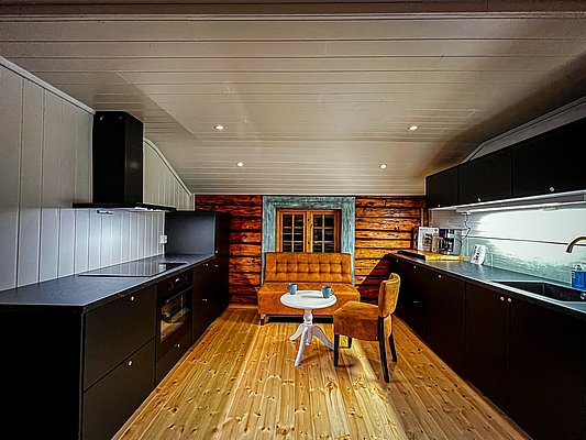 Gemütliche, moderne Küche in rustikaler Blockhütte auf Hitra, Norwegen. Dunkle Arbeitsflächen, Holzverkleidung, einladender Sitzbereich. Ideal für einen entspannten Angelurlaub. Perfekte Mischung aus Tradition und Komfort.