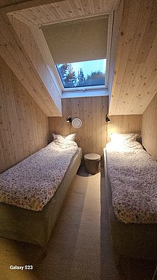 Gemütliches Schlafzimmer in Hitra, Norwegen. Zwei Einzelbetten unter einem Dachfenster mit Blick auf die Natur. Holzwände sorgen für eine warme Atmosphäre und laden nach einem erfolgreichen Angeltag zum Entspannen ein. Ideal für Angelurlaub.