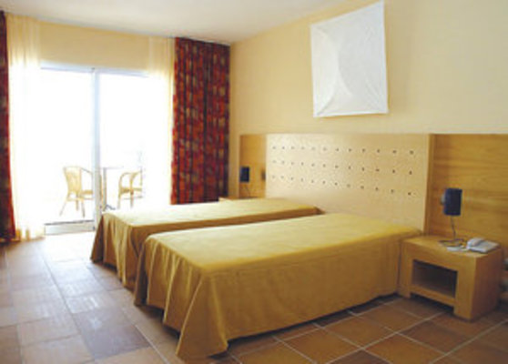 Ein helles Hotelzimmer mit zwei Einzelbetten, einem Holzmöbelset, und einem Balkon mit Blick auf den Außenbereich. Ein helles Hotelzimmer mit zwei Einzelbetten, einem Holzmöbelset, und einem Balkon mit Blick auf den Außenbereich.