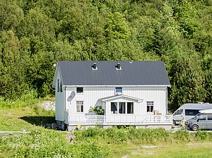 Weißes Holzhaus in Nordland, Norwegen, umgeben von grüner Natur. Perfekt für Angelurlaub und Erholung. Zwei geparkte Fahrzeuge, Sommerstimmung. Einladende, ruhige Landschaft für Abenteuer und Entspannung.