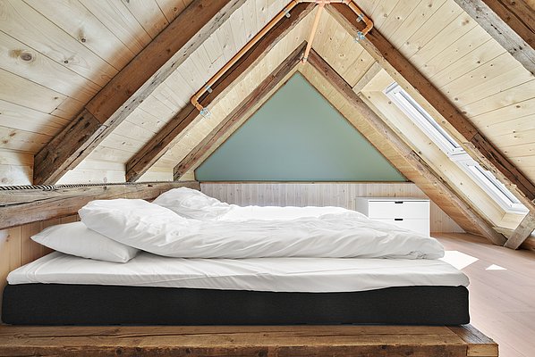 Gemütliches Dachgeschosszimmer in Südwest-Norwegen: Holzbalken, weißes Bett, Fenster mit natürlichem Licht. Ideal für entspannende Angelreisen und naturnahe Erholung. Skandinavisches Design trifft auf traditionelle Gemütlichkeit.