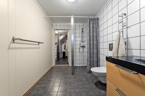 Modernes Badezimmer in Nord-Norwegen mit Duschbereich, Waschbecken und WC. Helle Wände und Fliesen erzeugen ein freundliches Ambiente. Perfekt für komfortable Angelurlaube in Norwegen.