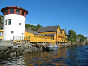 Gelbe Häuser und ein weißer Turm am Wasser in Südwest-Norwegen. Malerische Küstenlandschaft, ideales Ziel für Angelurlaub und Erholung. Klare blaue Himmel, ruhiges Wasser und beeindruckende Natur. Perfekt für Abenteuer und Entspannung.
