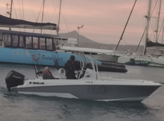 Ein modernes, weißes Anglerboot auf dem Meer von São Vicente, Kapverden, vor malerischer Kulisse mit Segelbooten und Bergen im Hintergrund bei Sonnenuntergang. Perfekt für Angelreisen und Abenteuer auf hoher See.