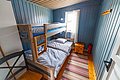 Gemütliches Schlafzimmer in Hitra, Norwegen: Holzbett mit Etagen, blauer Holzwandanstrich, Fenster mit Vorhang, bunte Teppichstreifen. Ideale Unterkunft für Angelurlauber, die Komfort und Nähe zur Natur suchen. Optimal für Angelreisen gestaltet.