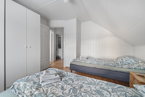 Gemütliches Schlafzimmer in Nord-Norwegen: Helle Holzwände, zwei Einzelbetten mit gemusterten Bezügen, Kleiderschrank, Holzfußboden. Ideal für Angelreisen, um nach erfolgreichen Tagen in der nordischen Natur zu entspannen.
