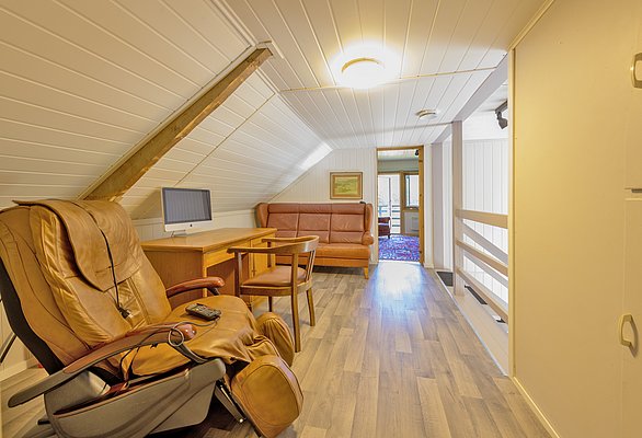 Gemütlicher Dachboden in Nordland, Norwegen: Holzvertäfelung, Massagesessel, Schreibtisch mit Bildschirm, Ledersofa. Helle, einladende Atmosphäre perfekt zum Entspannen nach einem erfolgreichen Angelausflug. Ideal für Angelreisen und erholsamen Rückzug.