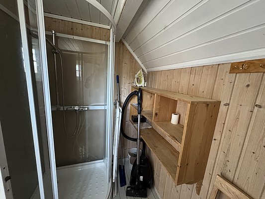 Gemütliches Badezimmer in Hitra, Norwegen: Holzwände, Dusche mit transparenter Tür, Stauraumregal, Staubsauger. Perfekt für Angelurlauber, die Komfort in skandinavischer Umgebung suchen. Nahe am Wasser, ideal für entspannte Erholung nach abenteuerlichen Angelausflügen.