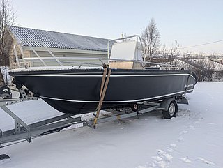 Schwarzes Motorboot auf Anhänger im verschneiten Südwest-Norwegen. Perfekt für Angelreisen und Meeresangeln. Winterliche, ruhige Kulisse, idealer Startpunkt für Angelabenteuer. Angelurlaub, Abenteuerlust, Natur pur.