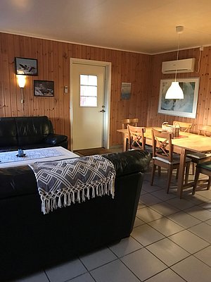 Gemütliches norwegisches Ferienhaus mit Holzwänden auf Hitra, Norwegen. Der Wohnbereich bietet eine komfortable Ledercouch, Holztisch mit Stühlen und skandinavische Dekoration – idealer Rückzugsort für Angler nach einem Tag auf See.