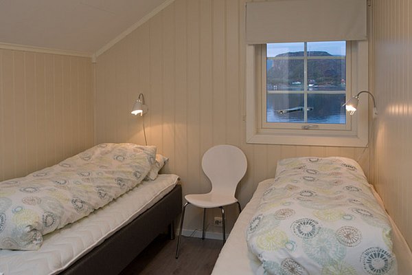 Gemütliches Schlafzimmer mit zwei Einzelbetten, dekoriert mit gemusterten Bettdecken, und einem Fenster mit Blick auf einen See und Berge.
