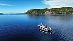 In der Region Hitra, Norwegen: Angler in Motorboot genießen ruhigen, blauen Fjord bei sonnigem Wetter. Landschaft mit bewaldeten Hügeln und klarem Himmel verspricht ideale Bedingungen für Angelabenteuer. Perfekter Angelurlaub in skandinavischer Idylle.