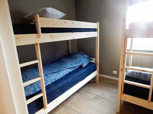 Gemütliches Schlafzimmer mit Holzetagenbetten und blauen Bettbezügen in einer Unterkunft in Nordland, Norwegen. Ideal für Angelurlauber, die Komfort und Abenteuer suchen. Helles, einladendes Ambiente für erholsame Nächte nach erfolgreichen Angeltouren.