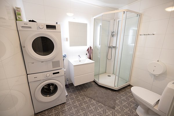Modernes Badezimmer in Nordland, Norwegen: Waschmaschine, Trockner, geräumige Dusche, Waschbecken mit Spiegel und WC. Helle Fliesen und stilvoller Bodenbelag sorgen für ein sauberes, einladendes Ambiente. Ideal für komfortable Angelreisen-Unterkünfte.