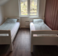 Gemütliches Schlafzimmer in Nordland, Norwegen, mit zwei Einzelbetten und rustikalem Charme. Helle Fenster bieten Ausblick auf die ruhige, grüne Landschaft. Ideal für erholsame Angelurlaubstage.
