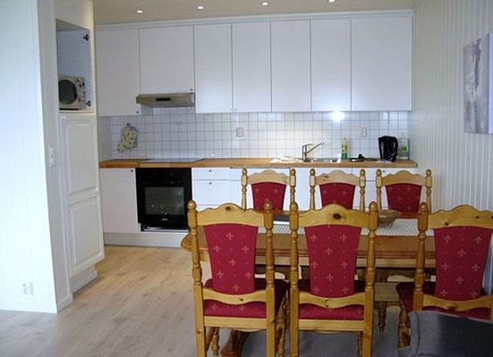 Gemütliche Küche in Nordland, Norwegen, mit weißem Küchenschrank, Holztisch und roten Stühlen. Helle, einladende Atmosphäre für erholsamen Angelurlaub. Ideal für Zubereitung frischer Fänge nach erfolgreichen Angelausflügen. Perfekter Rückzugsort zum Entspannen.